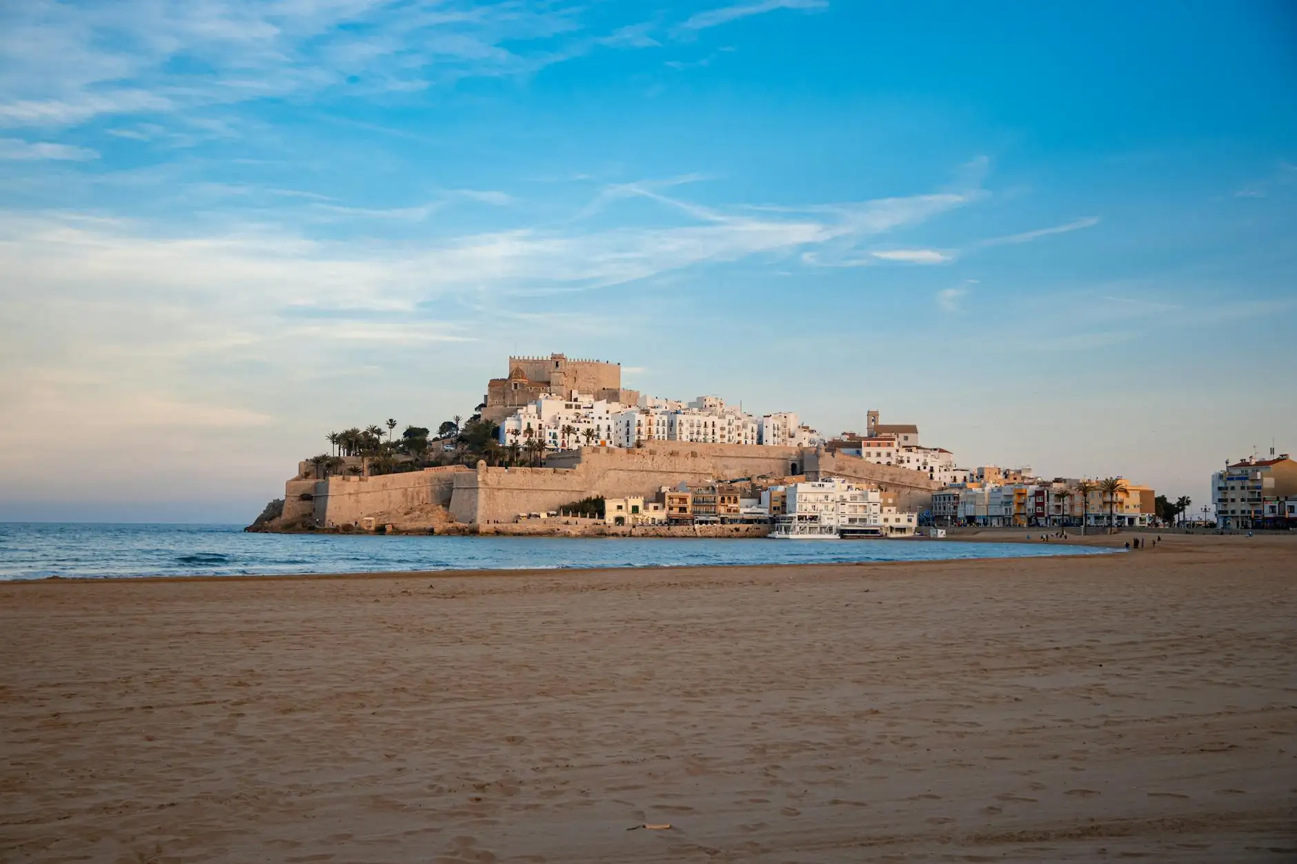 Serene landscape featuring Peñíscola Castle with a vast sandy beach and blue sky.