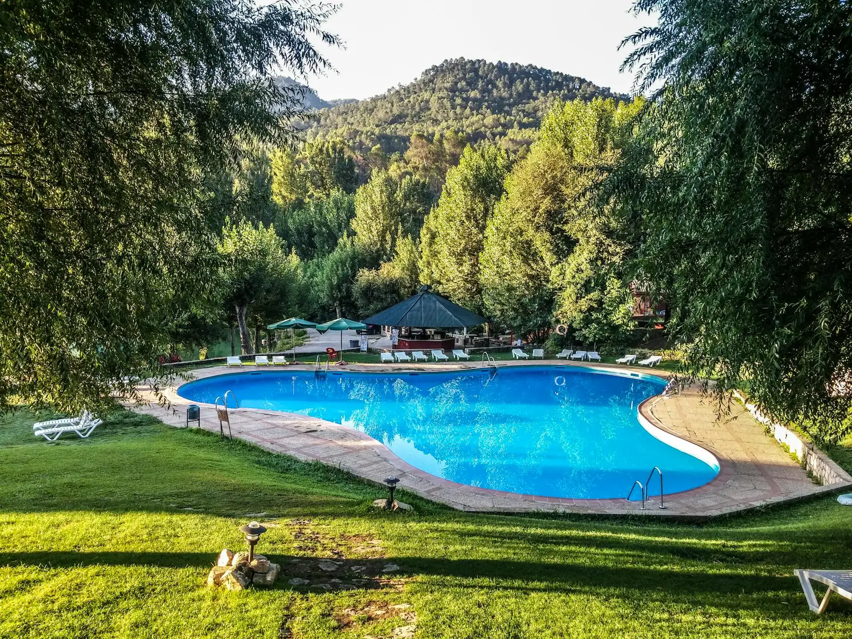 Relax at a luxury resort pool surrounded by lush greenery and scenic hills in Jaén, Spain.