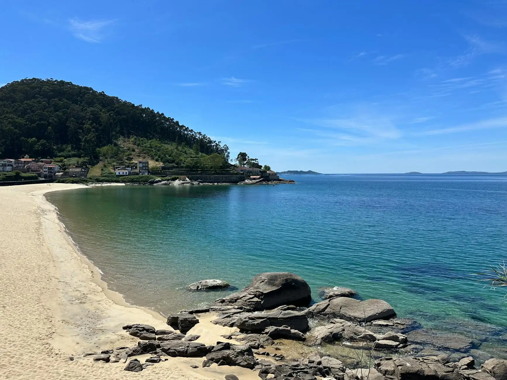 Explore a tranquil beach with clear blue waters and rocky coast in Galicia, Spain, ideal for a summer getaway.