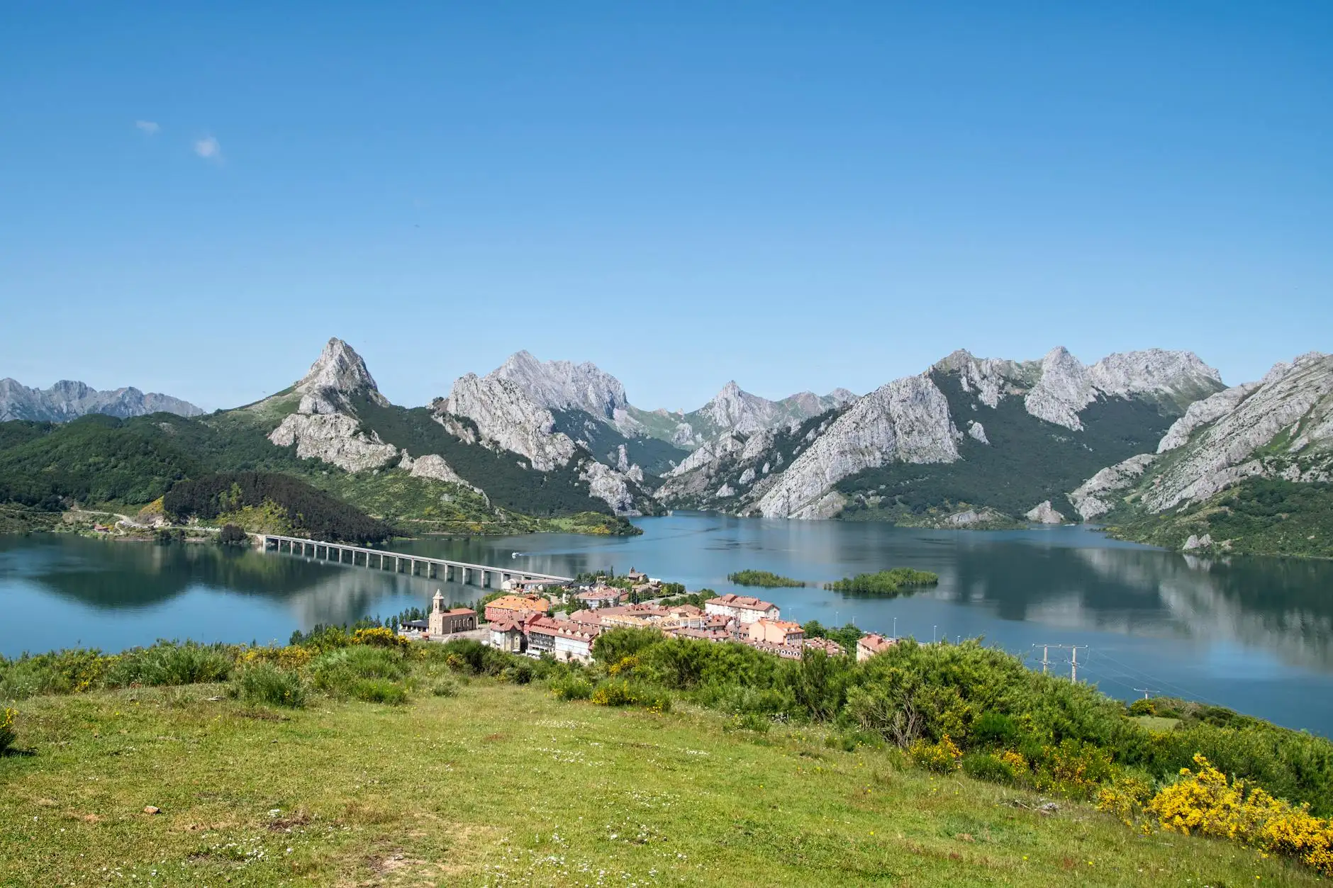 A breathtaking view of Riaño Reservoir with majestic mountains under a clear blue sky, perfect for travel enthusiasts.